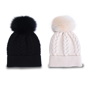 Dettaglio di berretti in maglia neri e beige con trecce e grandi pompon in finta pelliccia