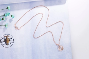 Detail of rose gold necklace with zircon-encrusted ring pendant and metal leaf accent