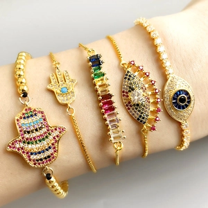 Detail of stacked gold-plated bracelets featuring Hamsa hand and Evil Eye charms