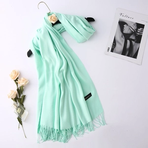 Detail of mint green cashmere scarf with fringe and label on a black hanger