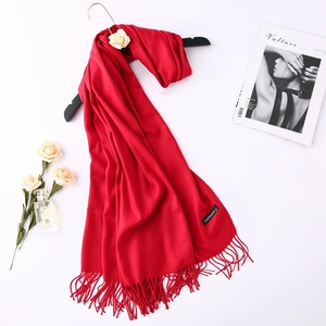 Detail of red cashmere scarf with fringe tassels hanging on a hanger with lifestyle props