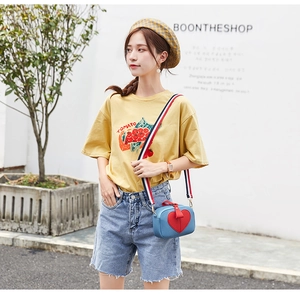 Detail of blue crossbody bag with red heart patch and striped ribbon shoulder strap