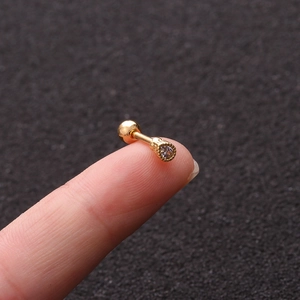 Macro shot of a tiny gold screw back earring with a clear zircon held on a fingertip