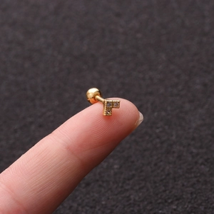 Macro shot of tiny gold T-shaped stud earring with zircon stones on a fingertip