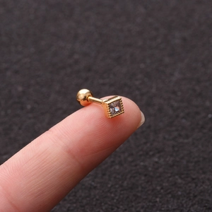 Macro shot of a golden flower stud earring with square zircon on a fingertip