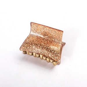 Macro view of golden glitter acrylic hair claw clip with metallic spring and teeth detail