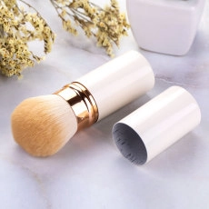 Detail of portable retractable powder brush with golden metal accents on marble surface