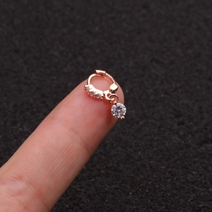 Macro detail of rose gold cartilage earring with zircon stones held on a fingertip