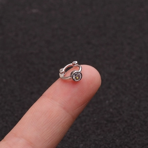 Macro shot of silver cartilage earring with zircon on fingertip showing small scale