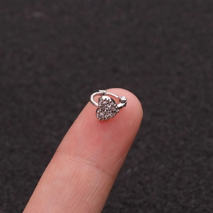 Macro view of a small heart-shaped silver ear cuff with cubic zirconia on a fingertip