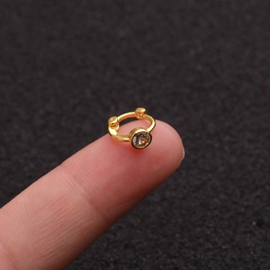 Close-up of a small gold hoop earring with clear zircon crystal on a fingertip