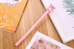 Close-up of pink cartoon gel pen featuring a 3D silicone bear topper on a wooden desk