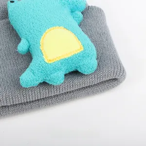 Close-up of a grey knitted children's hat with a 3D mint green plush dinosaur doll