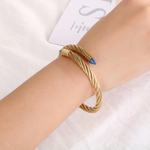 Gold-plated twisted cable open bangle with blue cone accents on a woman's wrist