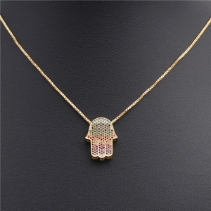 Detail view of a gold Hamsa hand pendant with rainbow cubic zirconia on a black mannequin