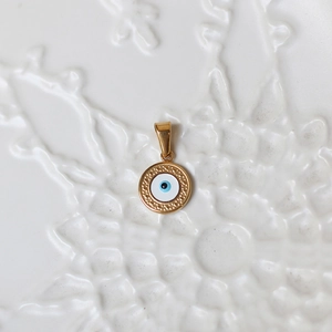 Macro view of a round 18K gold evil eye pendant with blue enamel and textured gold border
