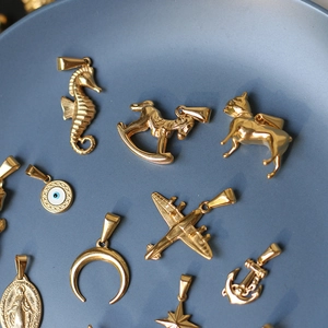 Detailed view of assorted 18K gold-plated stainless steel charms on a light blue tray