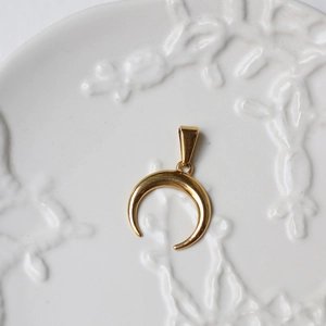 Detailed macro view of an 18K gold-plated crescent moon pendant on a ceramic tray