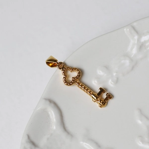 Detailed view of an 18K gold-plated key pendant on a vintage white ceramic tray