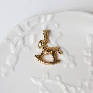 Macro shot of 18K gold rocking horse pendant on a white embossed ceramic plate