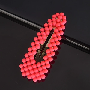 Detail view of coral pink pearl hair clip with textured beads on a black reflective surface