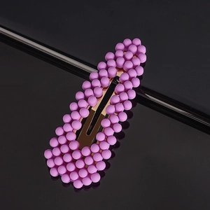 Detail view of pink matte beaded hair clip with a golden metal snap base on black surface