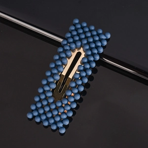 Close-up of a sweet blue beaded hair clip with golden metal base on black surface