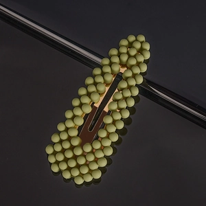 Macro shot of dusty green matte pearl hair clip with metal base on black reflective surface