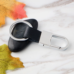 Premium black leather and silver metal keychain on marble surface with autumn leaves
