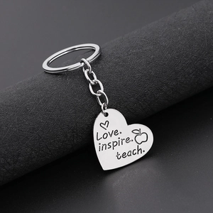 Macro shot of silver heart keychain engraved with Love. inspire. teach. on black stand