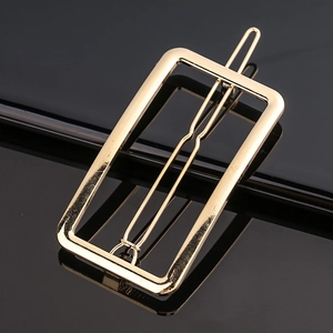 Macro d'une pince à cheveux rectangulaire dorée minimaliste sur une surface noire lisse