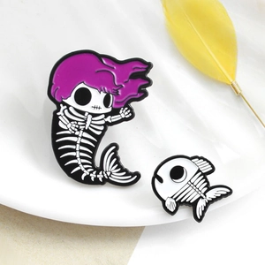 Macro view of mermaid skeleton and fish enamel pins with purple hair on a white plate
