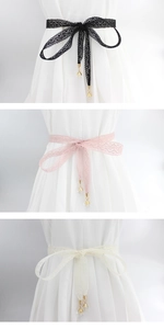 Detailed view of lace waist belts in black, pink, and beige with pearl and metal tassels