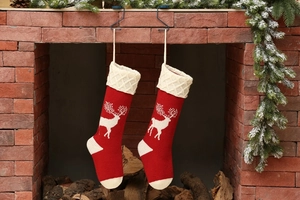 Close-up of red knitted Christmas stockings with white reindeer patterns by a cozy fireplace