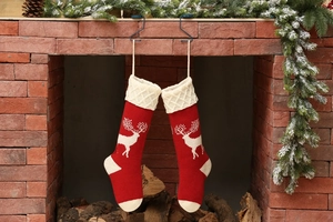 Detail of red cable knit Christmas stockings with white reindeer patterns on a fireplace