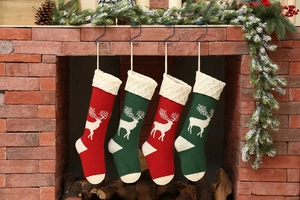 Close-up of four red and green knitted Christmas stockings with deer patterns on a fireplace