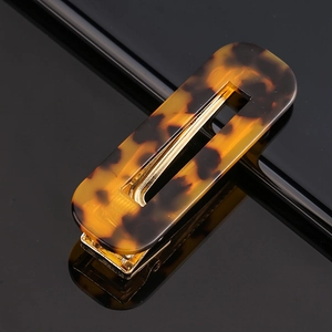 Macro shot of tortoiseshell acetate hair clip with gold metal base on black reflective surface