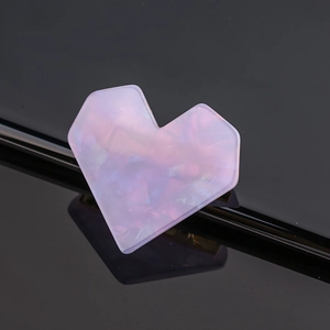 Macro shot of pink heart-shaped acetate hair clip with iridescent finish on black surface