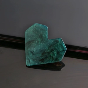 Macro detail of a dark green heart-shaped hair clip with shimmering glitter finish