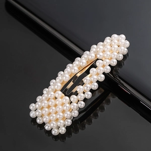 Detail of rectangular gold-tone hair clip with densely inlaid white pearls on black surface