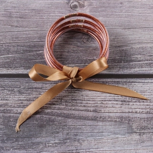 Close-up of five rose gold glitter filled silicone bangles with a decorative ribbon bow