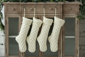 Vier cremefarbene Strick-Weihnachtssocken mit Rautenmuster hängen dekorativ an einem Schrank