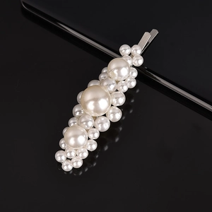 Detailed view of large and small pearls woven on a fishline bobby pin over black surface