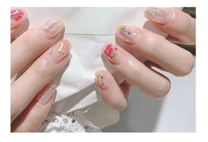 Detail of red dried flowers, gold lines, and shell flakes on elegant nail art design