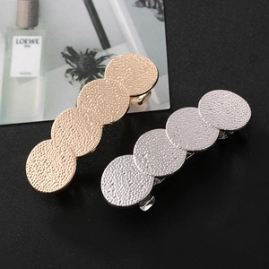 Détail de barrettes à cheveux avec cercles martelés or et argent sur fond texturé
