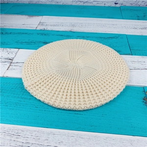 Beigefarbene Strickbaskenmütze mit Spiralmuster auf blauem Holzgrund präsentiert