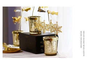 Close-up of golden rotating candle holder with glass cup featuring hanging snowflake charms