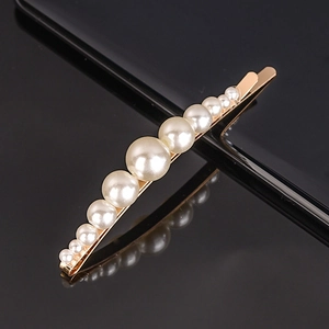 Detailed view of white pearls on a gold hair clip over a black reflective surface