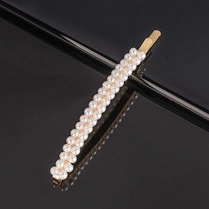 Detail of double-row white pearls on a gold-tone metal hair clip against black background