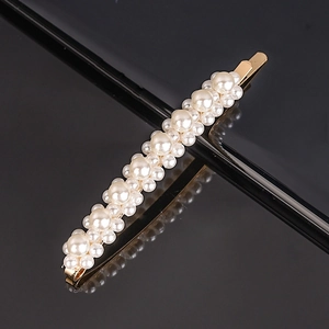 Close-up of golden alloy hair clip with white faux pearls and polished reflective surface